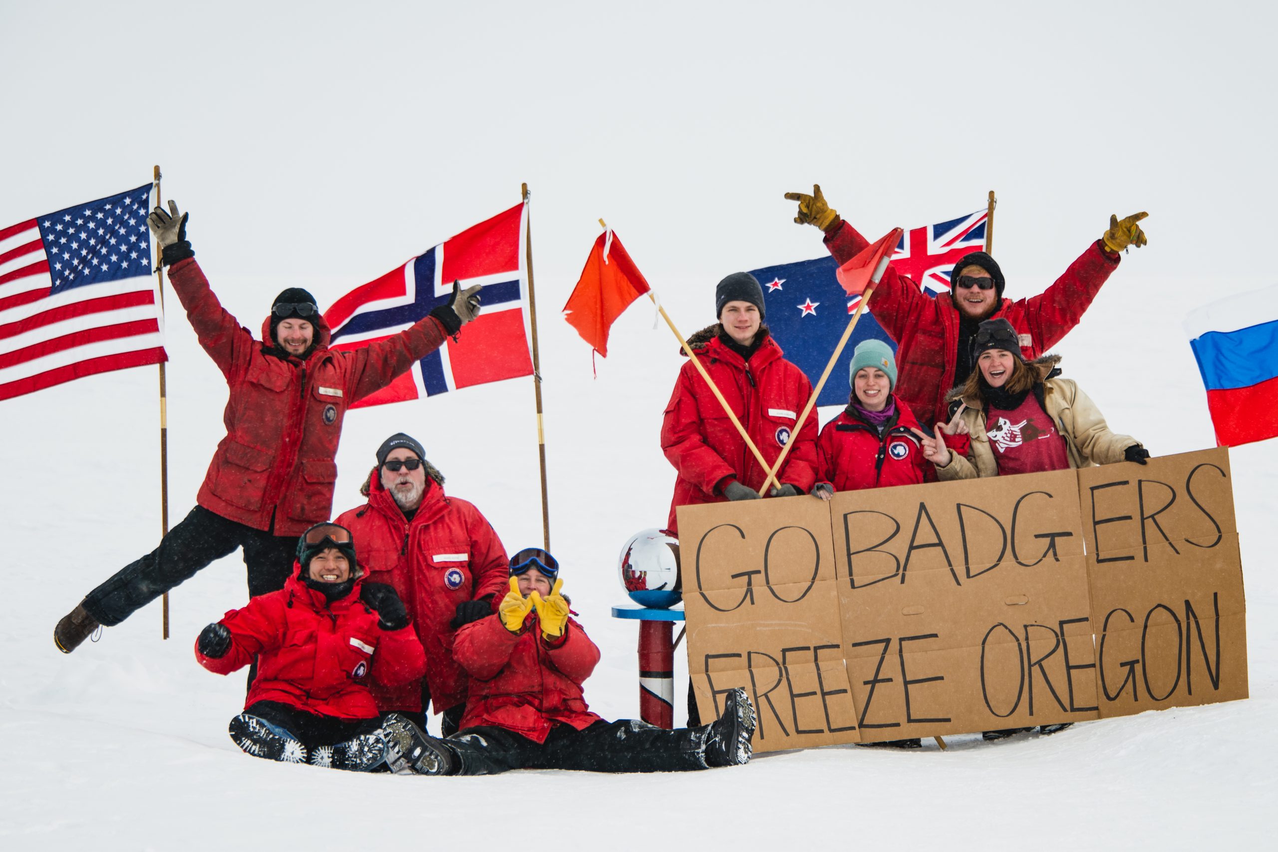 UW–Madison IceCube Laboratory researchers hold a sign that reads "Go Badgers, Freeze Oregon"